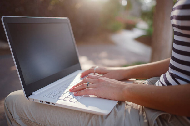 Female hands on laptop, woman types on keyboard sitting in park. Working outside and freelance concept, distance learning - 写真・画像
