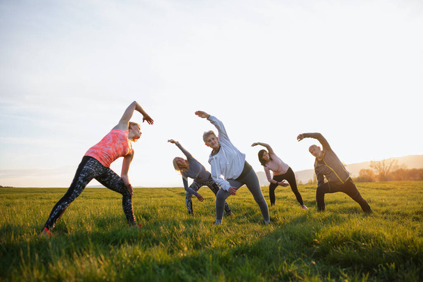 Group of seniors with sport instructor doing exercise outdoors in nature at sunset, active lifestyle. - Фото, зображення