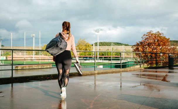 Spor çantalı, spor ayakkabılı, antrenmana gitmek için yürüyen tanınmayan bir sporcu. - Fotoğraf, Görsel