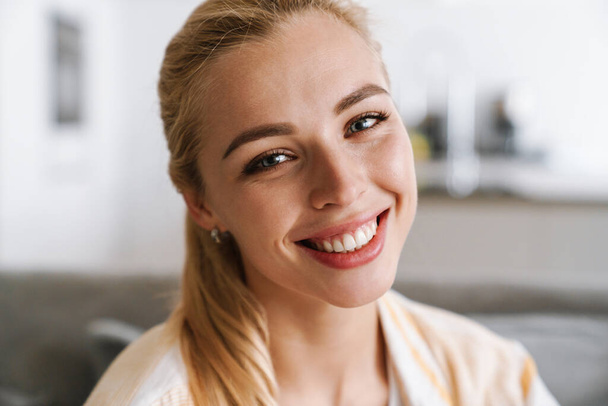 Happy blonde woman smiling and looking at camera at home - Fotó, kép