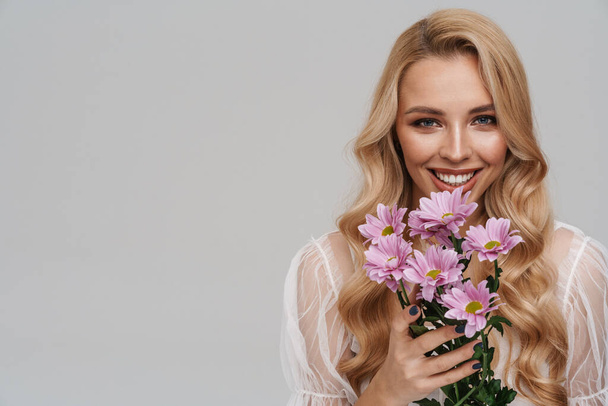 Beautiful happy girl smiling while posing with flowers isolated over grey background - Фото, зображення