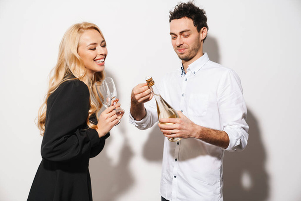 Feliz pareja romántica sonriendo mientras bebe champán aislado sobre fondo blanco - Foto, imagen