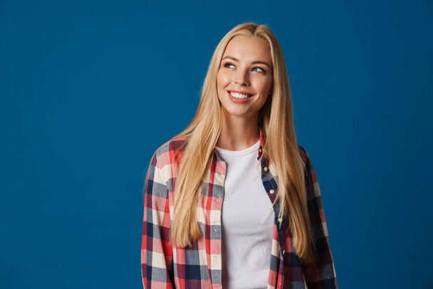 Blonde young happy woman smiling and looking aside isolated over blue background - Fotó, kép