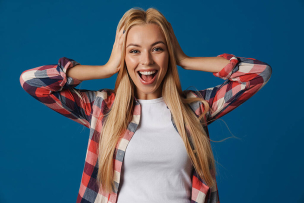 Blonde happy white woman smiling while holding her head isolated over blue background - Fotoğraf, Görsel