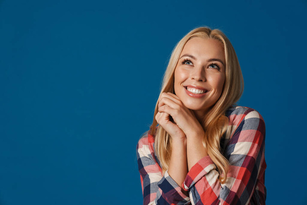 Blonde young happy woman smiling and looking upward isolated over blue background - Photo, Image