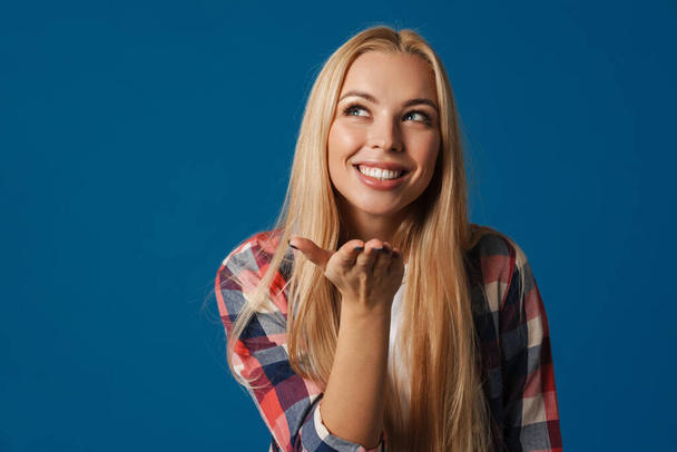 Blonde young happy woman smiling and holding copyspace isolated over blue background - Foto, imagen