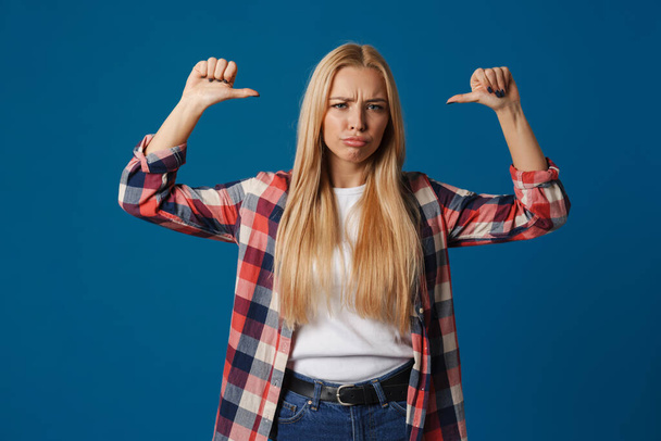 Blonde young displeased woman pointing fingers at herself isolated over blue background - Photo, image
