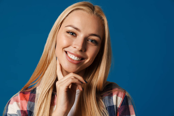 Blonde young happy woman smiling and looking at camera isolated over blue background - Фото, зображення