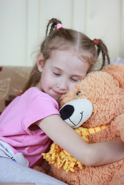portrait of a little girl in a pink dress with pigtails hugging a teddy bear, closed eyes from happiness and love - Photo, image