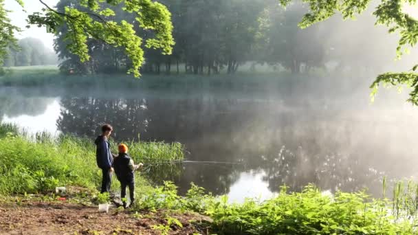 όμορφη τοποθεσία στη λίμνη πρωί ομίχλη παιδιά αλιείας με καλάμια ψαρέματος - Πλάνα, βίντεο