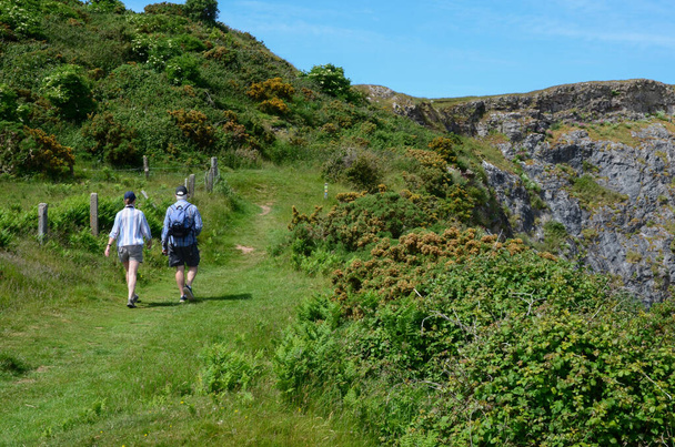 Llandudno, Reino Unido: 17 de junho de 2021: Caminhantes escalam um caminho até Little Orme em um dia ensolarado, no final da primavera. O caminho faz parte do Caminho da Costa de Gales de longa distância. - Foto, Imagem