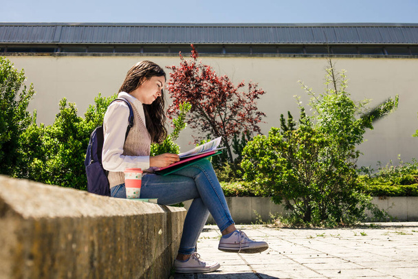 College student girl sitting in a campus park with books and bag. Shot from below - Fotografie, Obrázek
