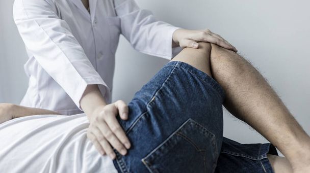 Fizjoterapia, fizjoterapeutka leczy ból nóg i bioder u mężczyzn uczęszczających do kliniki, układ kostny, niechirurgiczne leczenie, nowoczesne techniki medyczne. - Zdjęcie, obraz