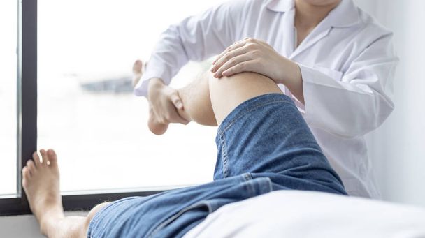 Fizjoterapia, fizjoterapeutka leczy ból nóg i bioder u mężczyzn uczęszczających do kliniki, układ kostny, niechirurgiczne leczenie, nowoczesne techniki medyczne. - Zdjęcie, obraz