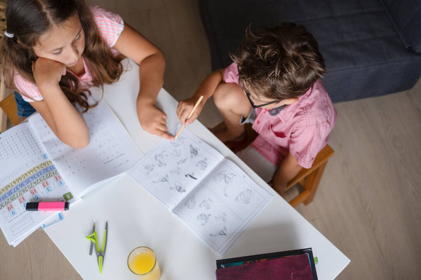 Симпатичные девочка и мальчик в очках, учится дома, сделать домашнее задание - Фото, изображение