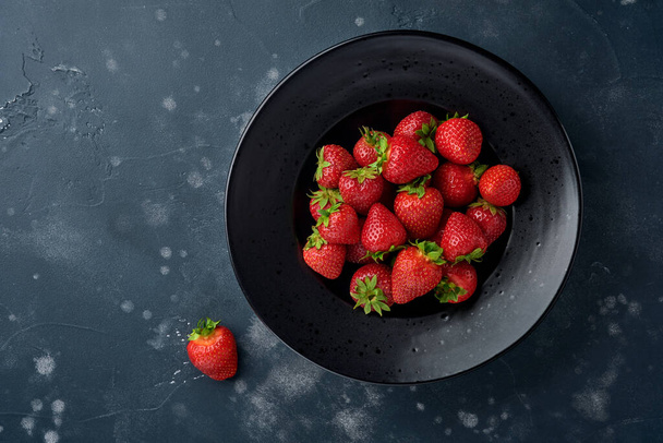 Still life with fresh strawberry in a black bowl. Top view photo of juicy strawberries.Healthy eating concept. Top view with copy space. - Фото, зображення