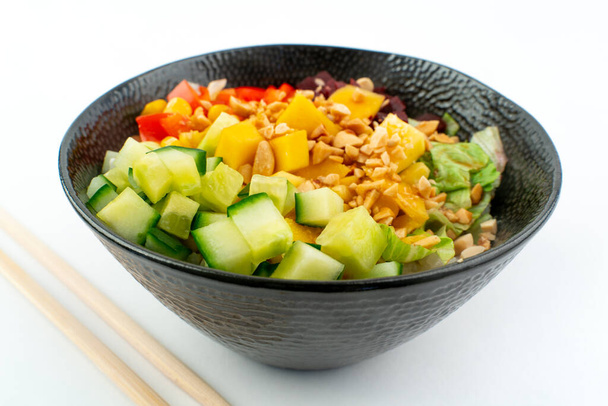 Poke bowl végétarien en forme de bol noir avec des baguettes ci-dessous, isolé sur fond blanc. Concombre vert, poivron rouge, arachides, maïs, betterave sur le riz sushi. Alimentation végétarienne saine - Photo, image