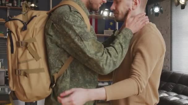 Powolne ujęcie homoseksualnego żołnierza w mundurze przytulającego i dotykającego czoła do swojego partnera w domu i żegnającego się przed rozmieszczeniem, a potem wychodzącego - Materiał filmowy, wideo