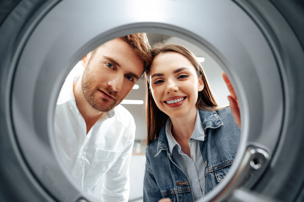 Happy couple choosing new washing machine in a store, view from the inside of washing machine - Foto, Bild