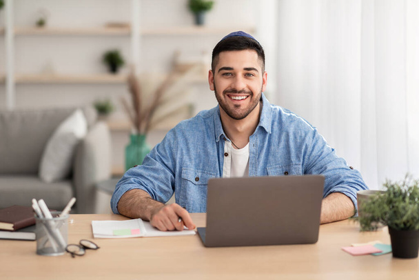 Uomo israeliano sorridente che lavora su laptop a casa - Foto, immagini