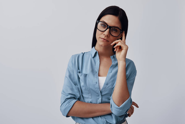 Attractive young woman in eyewear looking at camera while standing against grey background - Φωτογραφία, εικόνα
