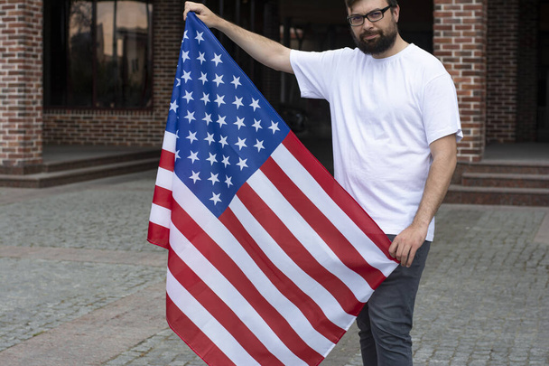 Young handsome man with glasses and a beard holding a USA flag and celebrating Independence Day - Valokuva, kuva