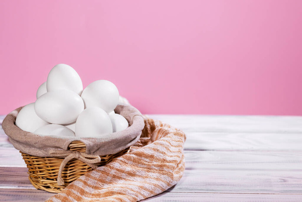 Fehér csirke tojásszin egy szalmakosár egy rózsaszín háttér-val darab ruha, természetes termék - Fotó, kép