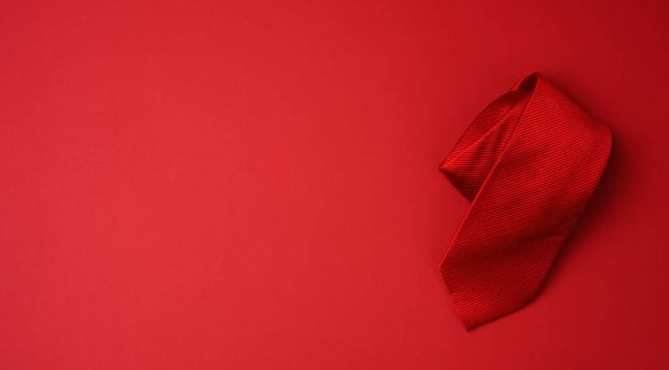 twisted silk red tie on a red background, copy space - Zdjęcie, obraz