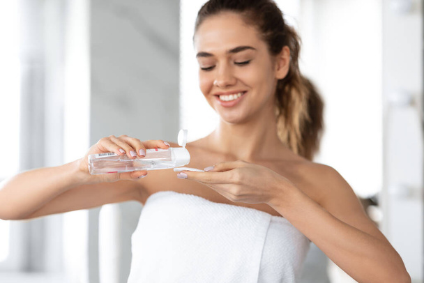 Весела леді наносить міцелярну воду на бавовняну тарілку у ванній
 - Фото, зображення