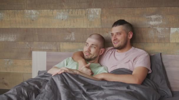 Handheld plan moyen de couple gay aimant se détendre dans le lit ensemble et bavarder tout en étreignant - Séquence, vidéo