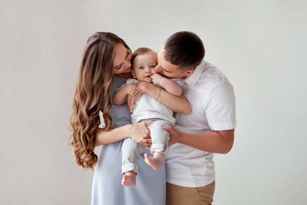 Happy young family. Beautiful Mother and father kissing their baby . Parents, Portrait of Mom, dad and smiling child on hands isolated over white background. - Photo, image