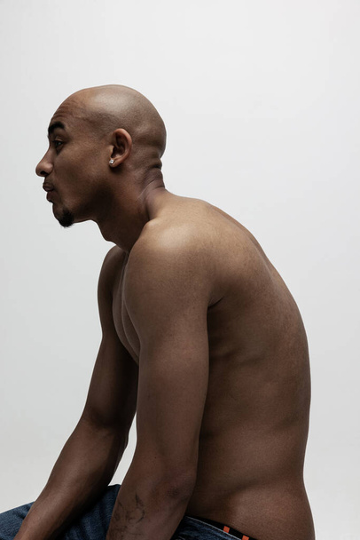 Seitenansicht. Ein junger muskulöser afrikanischer Mann posiert isoliert vor weißem Hintergrund. Konzept der Schönheit, Kosmetik, Wellness. - Foto, Bild