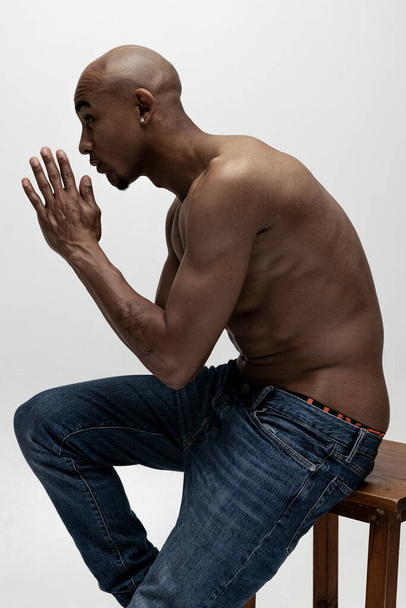 Seitenansicht. Ein junger muskulöser afrikanischer Mann posiert isoliert vor weißem Hintergrund. Konzept der Schönheit, Kosmetik, Wellness. - Foto, Bild