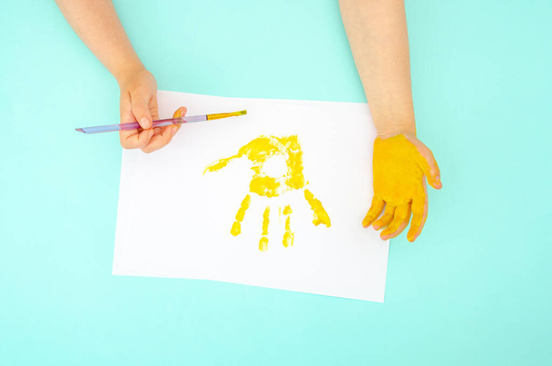 Детские ручки рисуют яркими красками на бумаге крупным планом. Детский отпечаток руки - Фото, изображение
