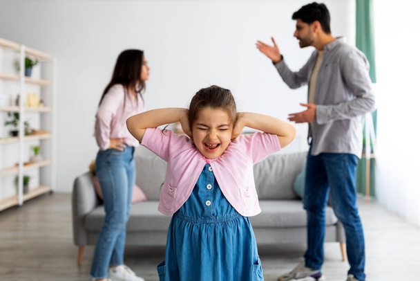 Rodinný argument. Plačící malá východní dívka zakrývající uši, aby neslyšela hádky rodičů, selektivní soustředění - Fotografie, Obrázek