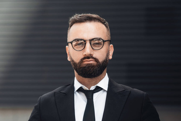 Business and entrepreneurship concept. Portrait of confident businessman in glasses and black suit looking at camera - Фото, изображение