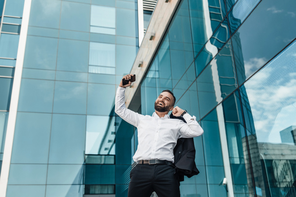 Liikevoitto. Komea liikemies kättelee nyrkkejä juhlii menestystä töissä, seisoo toimistorakennusta vastaan - Valokuva, kuva