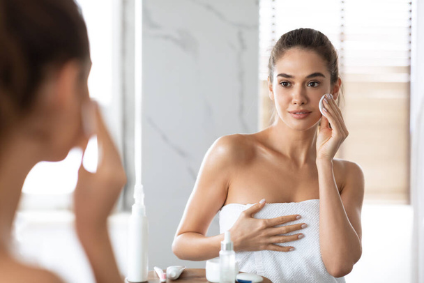 Femme utilisant coton tampon regardant miroir réflexion dans la salle de bain - Photo, image