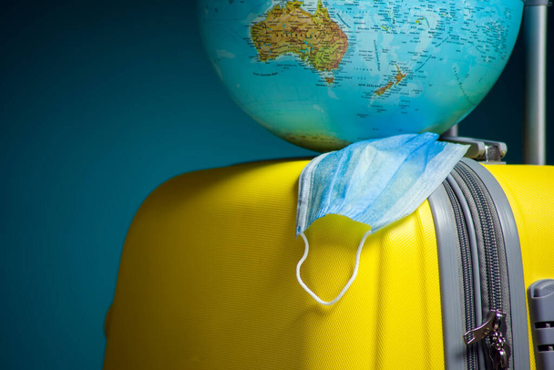 Глобус з медичною маскою для обличчя на багажі. Концепція подорожей та коронавірусу. Студійний знімок
 - Фото, зображення