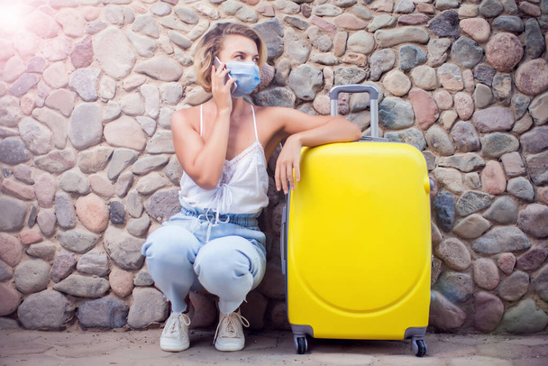 Mujer con equipaje con máscara facial médica y uso de teléfono inteligente al aire libre. Concepto de viaje y coronavirus - Foto, imagen