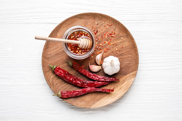 Plate with hot honey, garlic and dry chili peppers on light wooden background - Photo, Image
