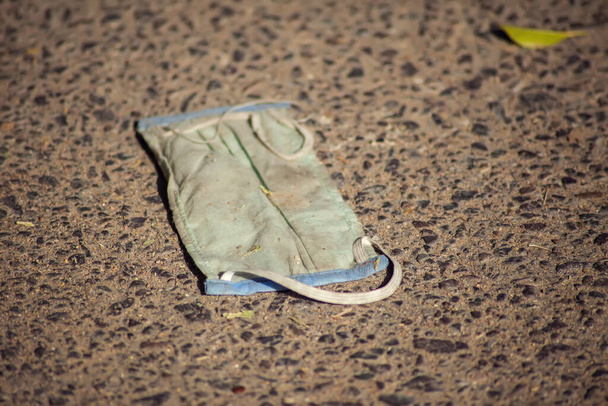Used medical face mask as a garbage on the ground outdoor. Environmental pollution concept - 写真・画像