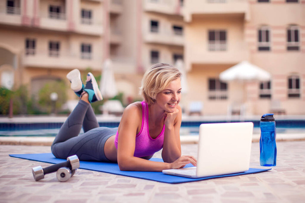 Молодая женщина, начинающая занятия фитнесом на открытом ноутбуке. Человек, спорт и здравоохранение - Фото, изображение