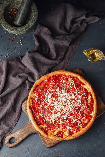 Plateau avec pizza savoureuse de style Chicago, épices et huile sur fond sombre - Photo, image