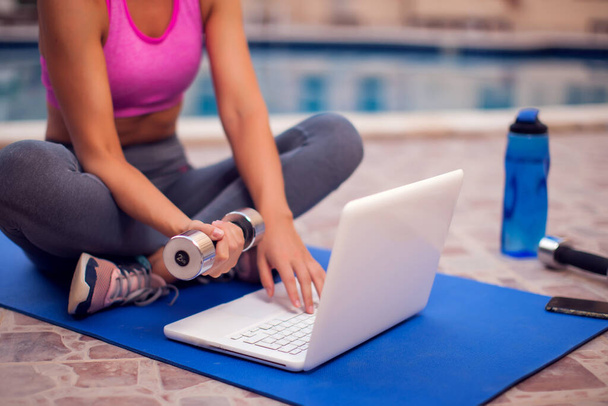 Mujer joven que comienza la clase de fitness en línea en un ordenador portátil al aire libre. Concepto de personas, deporte y salud - Foto, imagen