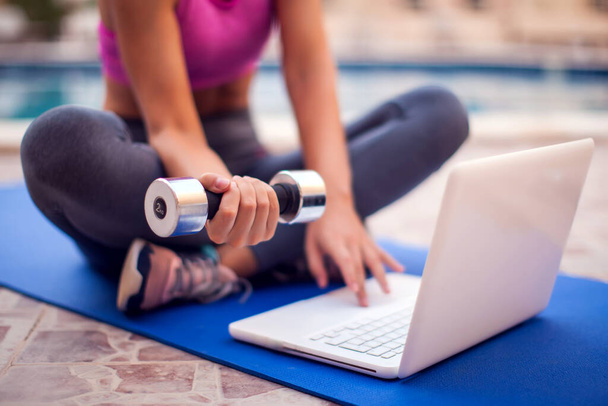 Młoda kobieta zaczynająca zajęcia fitness online na laptopie na świeżym powietrzu. Ludzie, sport i opieka zdrowotna - Zdjęcie, obraz