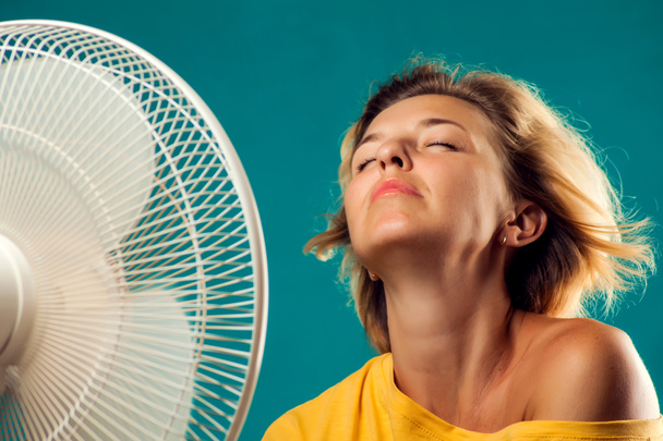 Un retrato de una mujer frente a un abanico que sufre de calor. Concepto de clima caliente - Foto, imagen