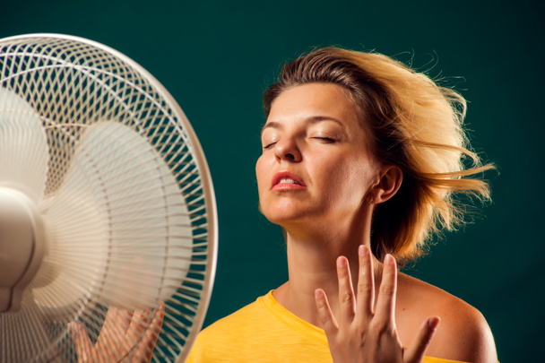 Un retrato de una mujer frente a un abanico que sufre de calor. Concepto de clima caliente - Foto, Imagen