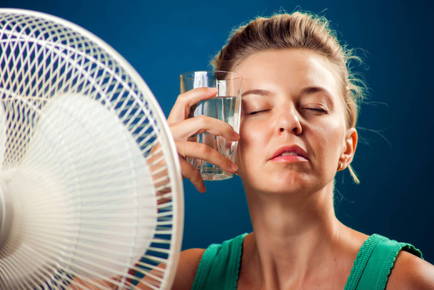 Muotokuva naisesta kuumuudesta kärsivän tuulettimen edessä. Kuuman sään käsite - Valokuva, kuva