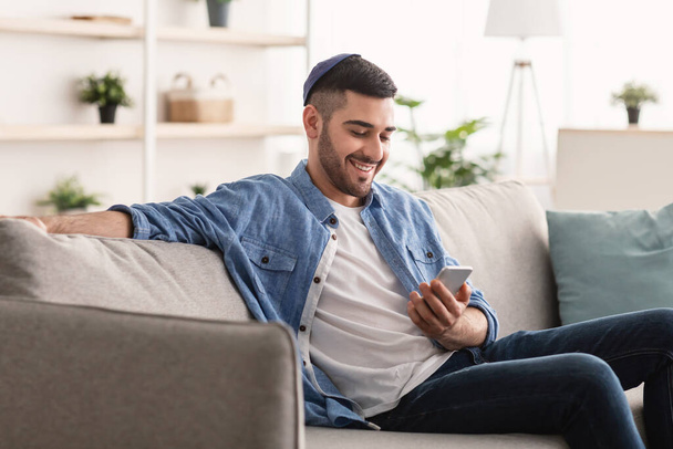 Primo piano dell'uomo ebreo sorridente che usa lo smartphone a casa - Foto, immagini